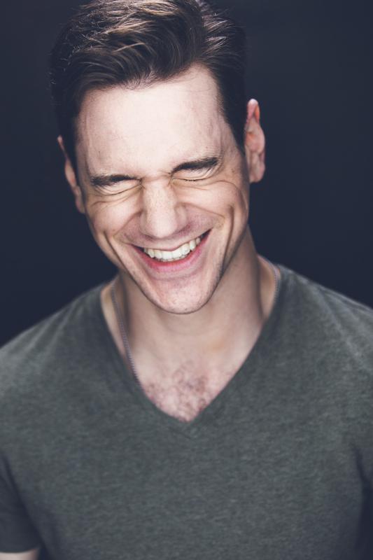 Michael Neal Johnson wears a green shirt and smiles in front of a black background.