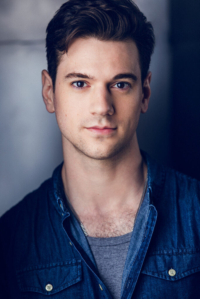 Michael Neal Johnson wears a blue shirt and stands in front of a light grey background.